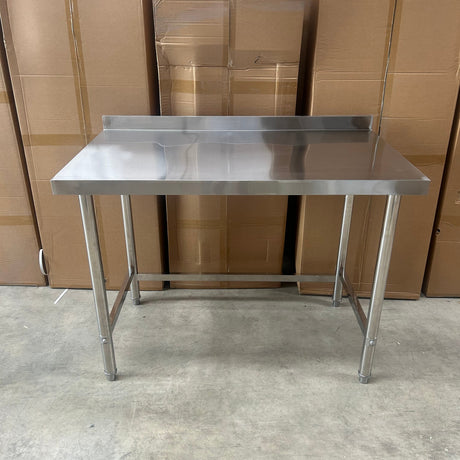 A 1200mm stainless steel utility table with a rectangular worktop and four legs, photographed in a warehouse setting with cardboard boxes stacked on the left and a concrete floor on the right.