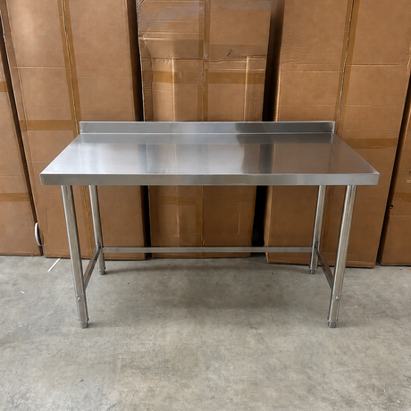A 1500mm stainless steel utility work table with a rectangular top and four legs, positioned in front of a stack of brown cardboard boxes on a concrete floor.