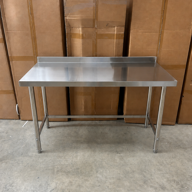 A 1500mm stainless steel utility work table with a rectangular top and four legs, positioned in front of a stack of brown cardboard boxes on a concrete floor.
